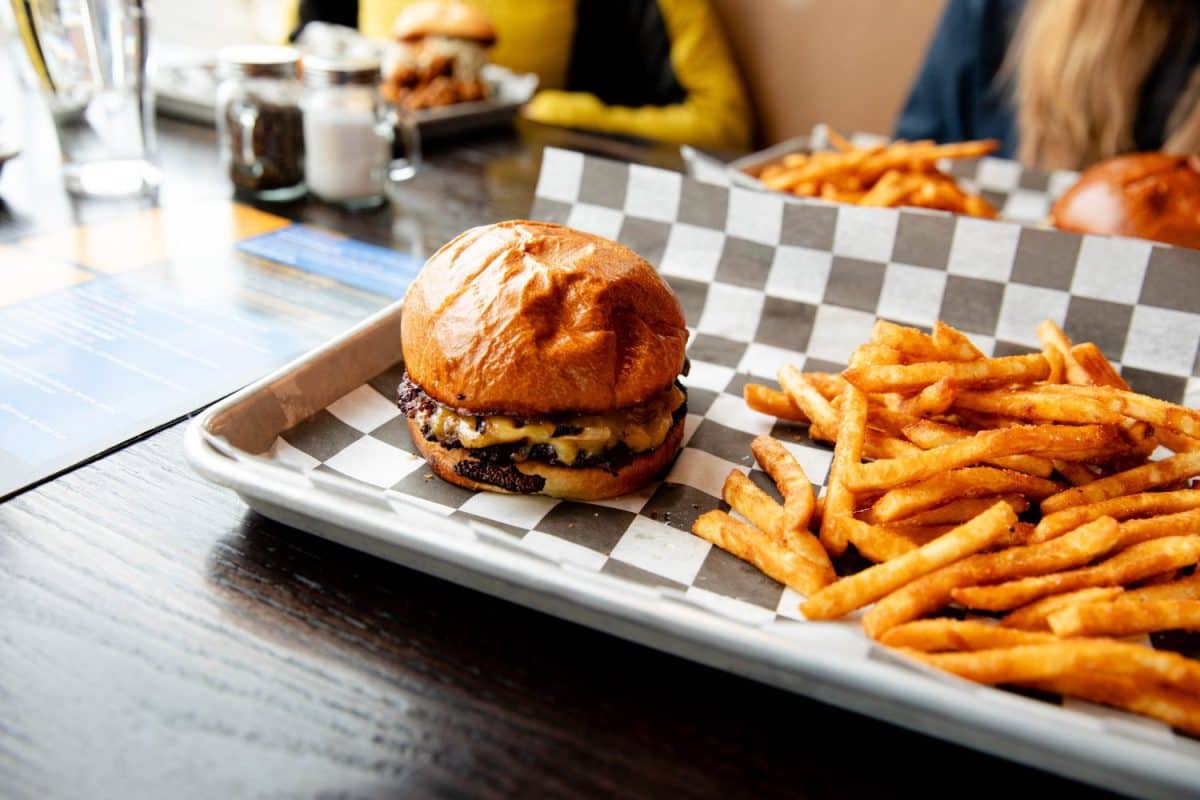 A delicious looking cheeseburger and french fries on on a tray with black and white checkered paper tray liner on a table in a fast food restaurant. American food. Hamburger with fries