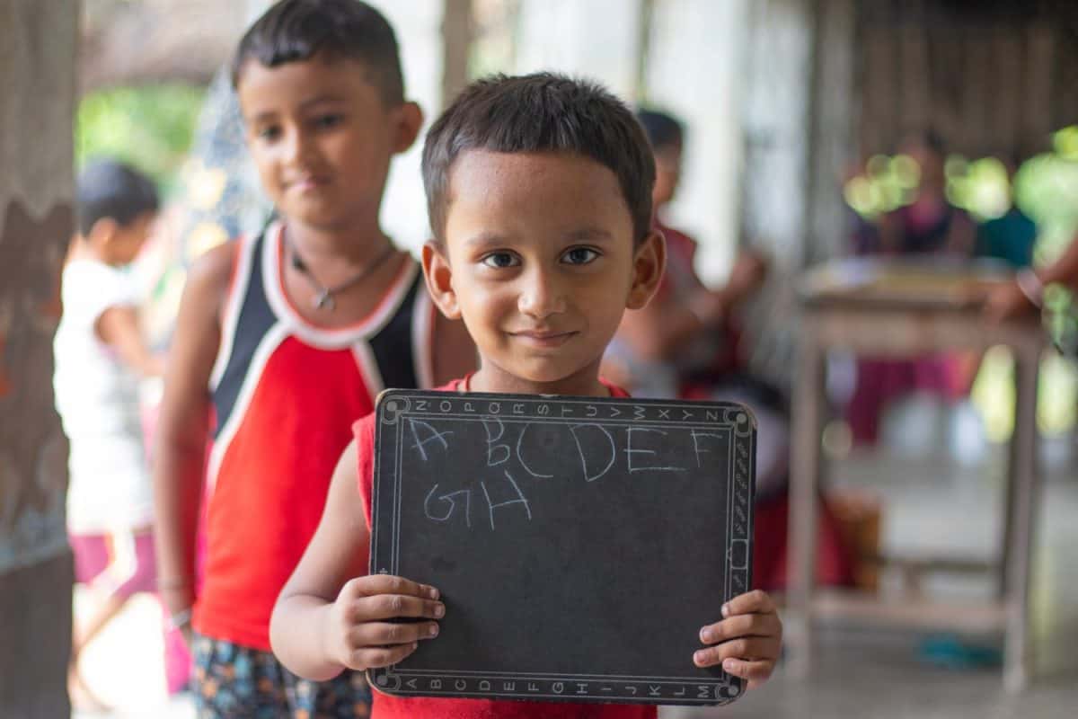 Smiling rural indian school boy Showing slate while standing his friend at school