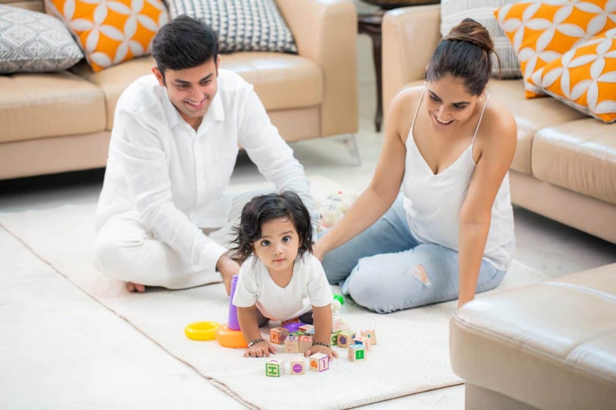 Parents watching their cute baby boy playing with toys on floor