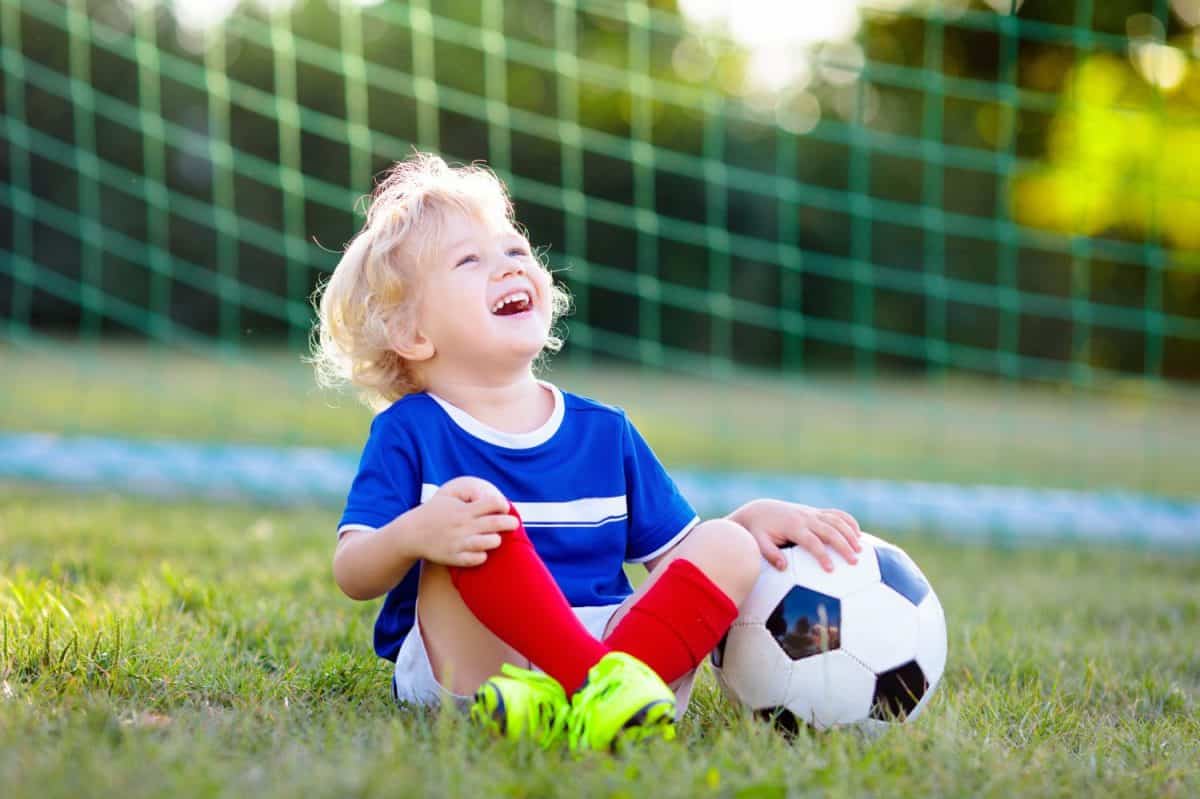 Kids play football on outdoor field. France team fans with national flag. Children score a goal at soccer game. Child in French jersey and cleats kicking ball. Fan celebrating victory at pitch.