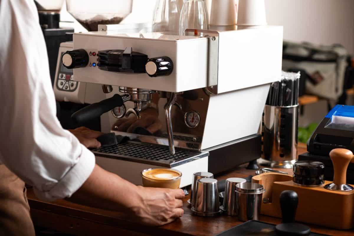 A barista prepares a latte at a professional espresso machine in a cozy coffee shop. The scene captures the meticulous process of brewing coffee, with various barista tools.