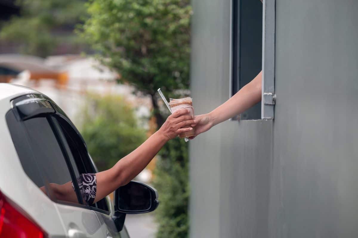 Hand Man in car receiving coffee in drive thru fast food restaurant. Staff serving takeaway order for driver in delivery window. Drive through and takeaway for buy fast food for protect covid19.