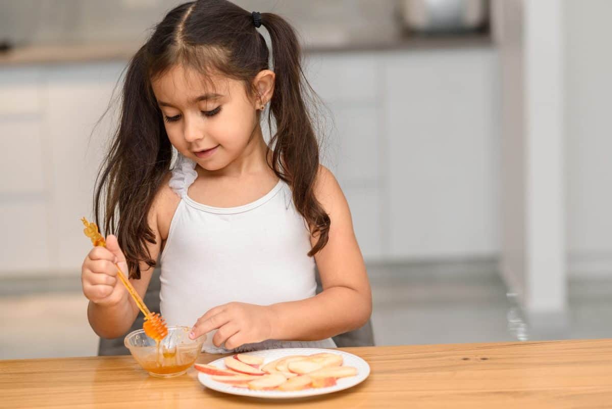 Little girl eating apple with honey. Symbol of the Jewish New Year Rosh HaShanah.