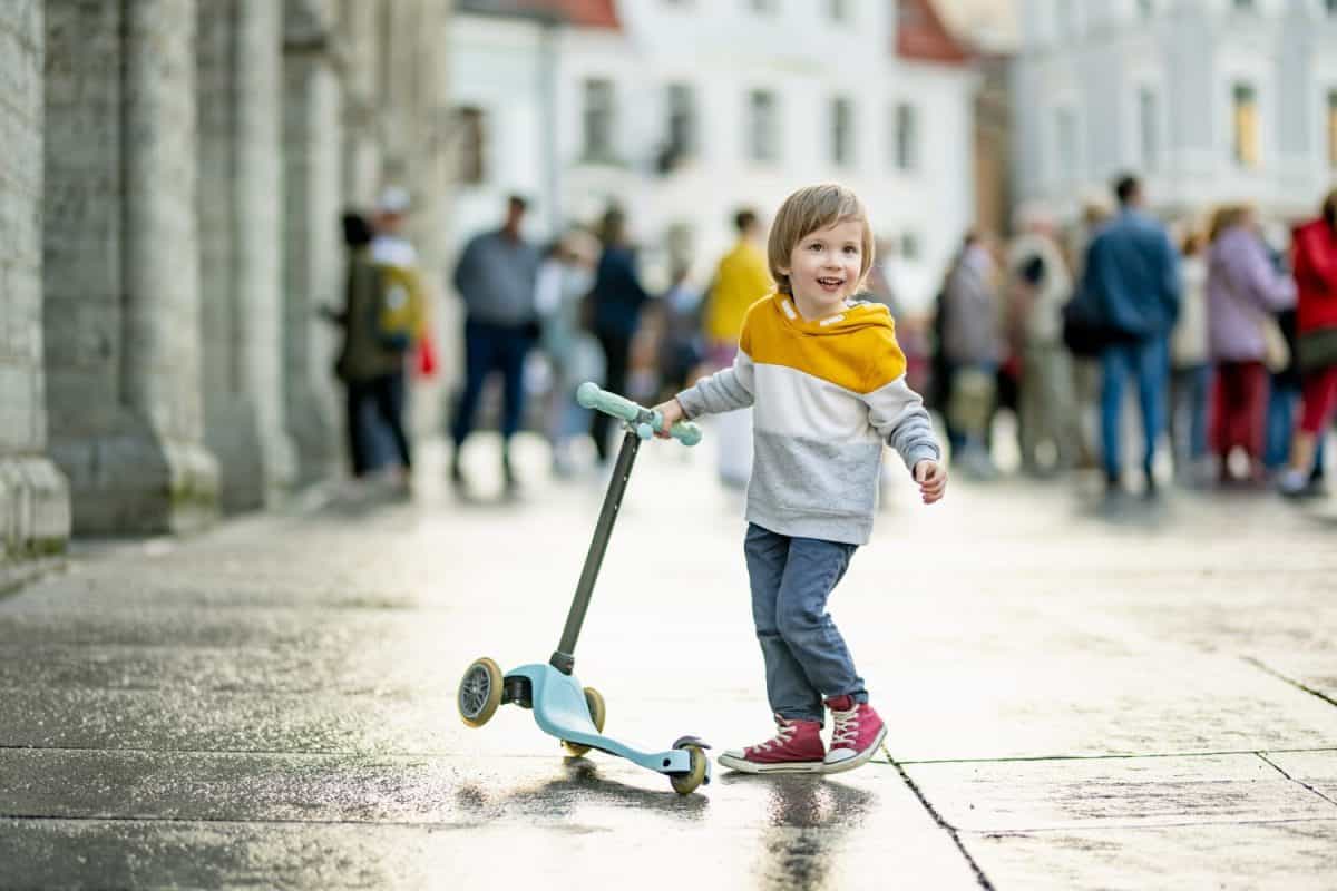 Cute little boy riding his baby scooter along colorful medieval streets of Tallinn Old Town or Tallinna Valalinn, included in the UNESCO World Heritage List. Child exploring Estonian capital.