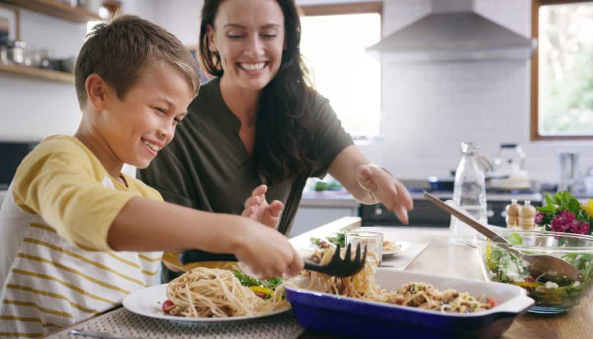 Happy people, child and serving dinner with kitchen, meal and food for holiday or vacation. Excited, woman and table with hungry as family, mom and kid for nutrition, bonding and healthy diet in home