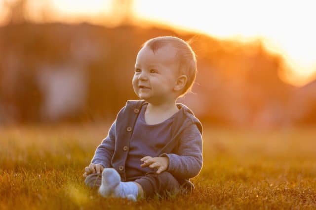 Baby boy sitting in grass smiling at sunset in backyard