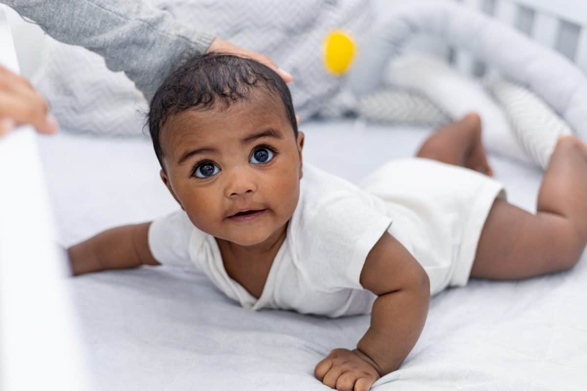 Mother playing with adorable newborn baby smiling and happy at home. Happy baby. African baby. Baby in the crib. Crib. Children's room.