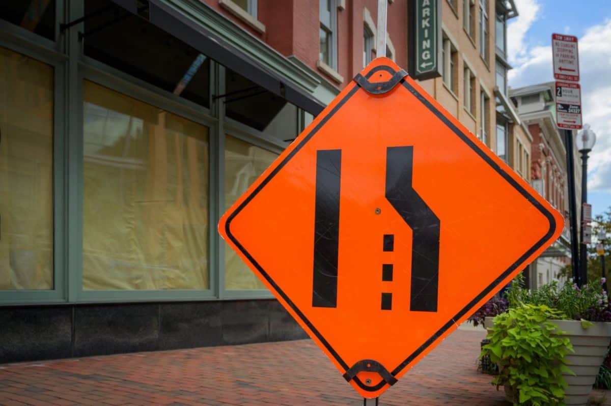 Large orange lane closed merge sign on urban sidewalk space for copy.