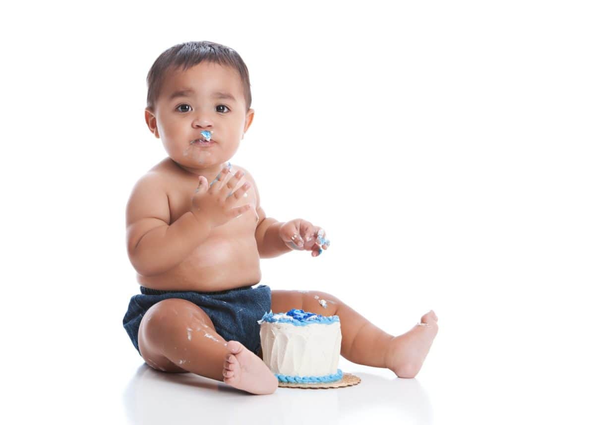 Birthday cake smash. Adorable baby boy eating a small birthday cake. Isolated on white.