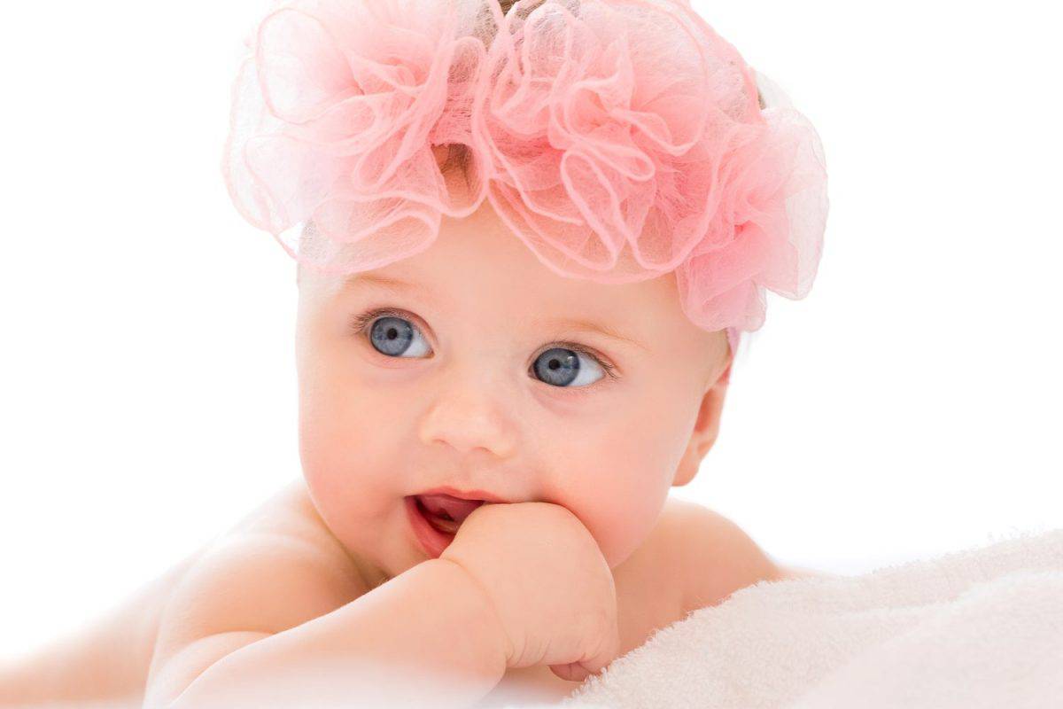 Cute little baby girl with big blue eyes and flower in her hair