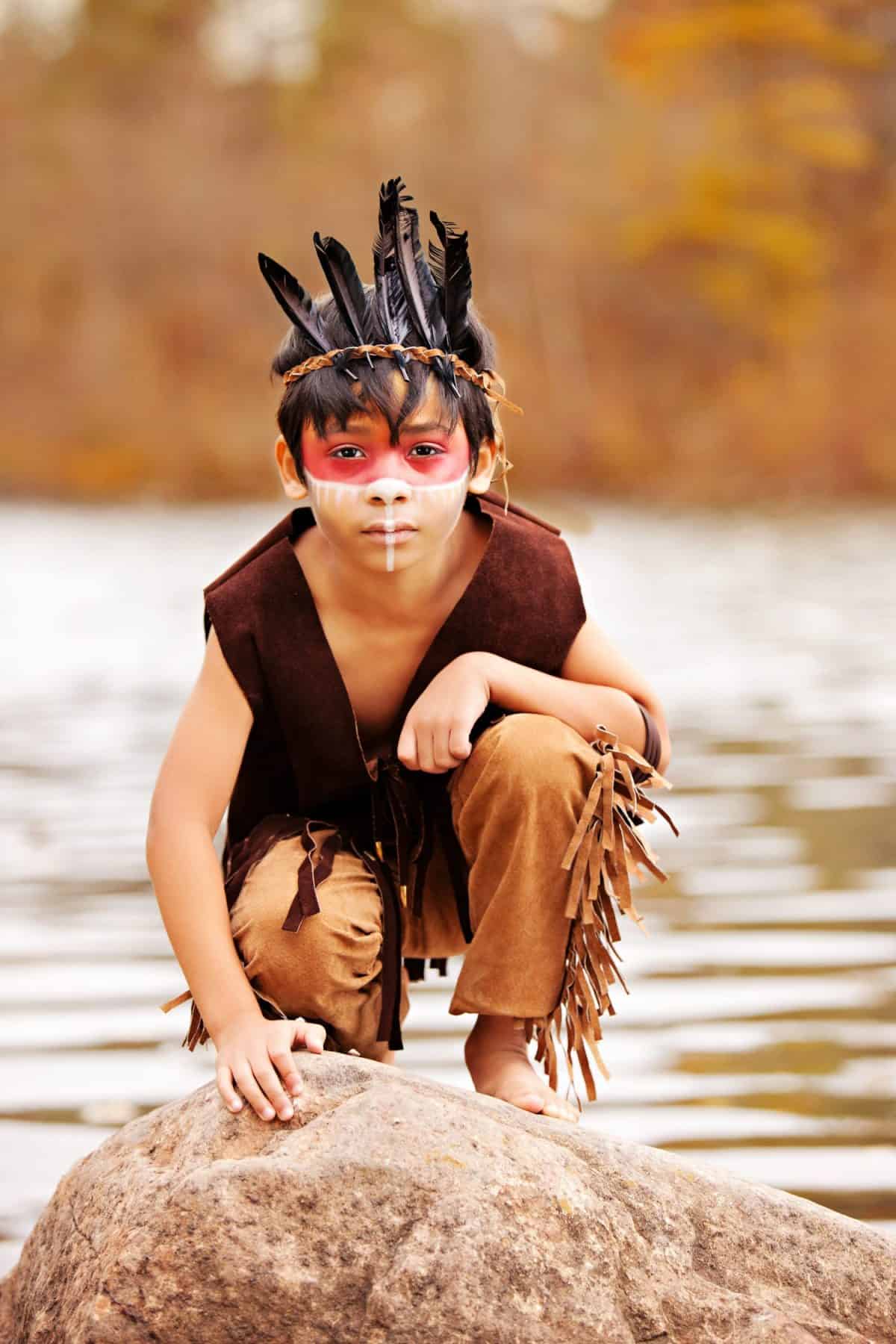 Young Native American. Adorable young boy dressed as a Native American squatting on a rock.