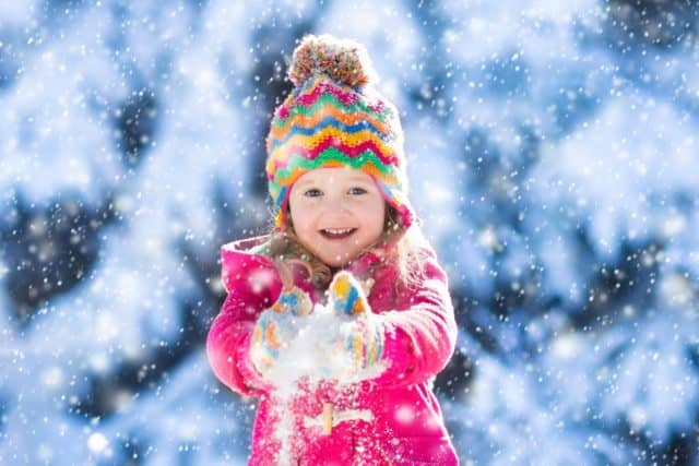 Child running in snowy forest. Toddler kid playing outdoors. Kids play in snow. Christmas vacation in sunny winter park for family with young children. Little girl in colorful jacket and knitted hat.