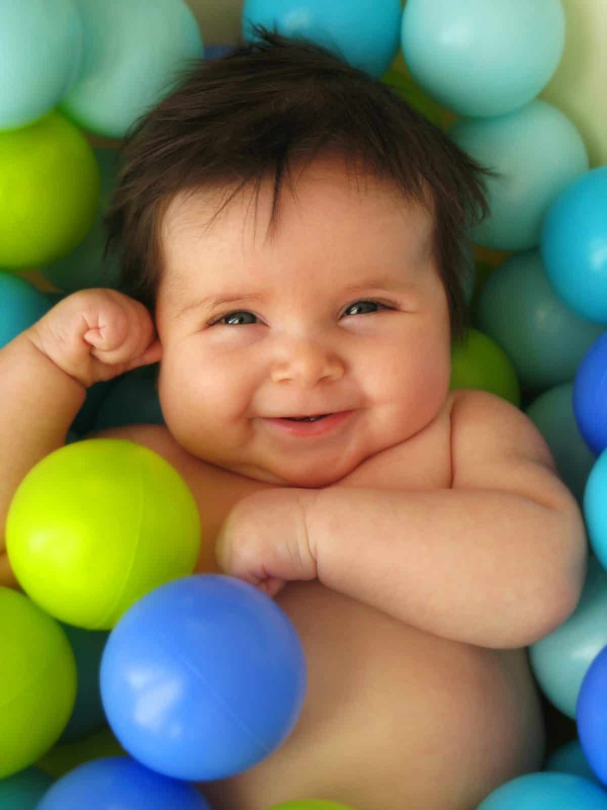 A happy 3 months old baby in a bath of balls.