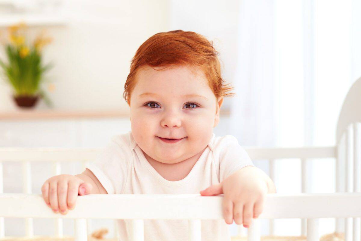 portrait of cute happy infant baby standing in a cot at home