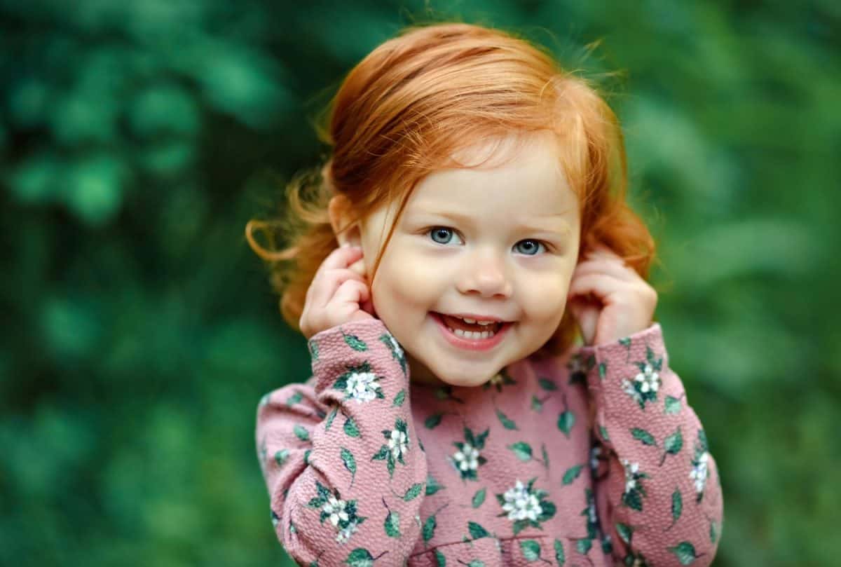 Little beautiful red-haired little girl smiling happily, in summer in the forest