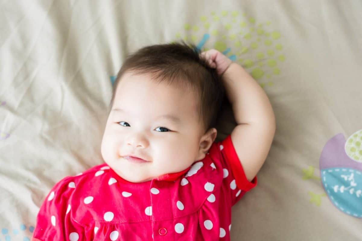 Portrait of adorable baby girl lying on back on the bed and looking in camera indoors