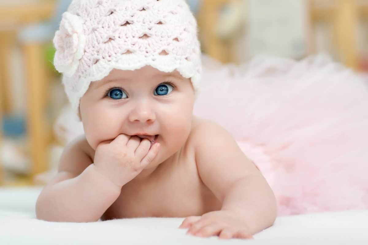 Charming child. Little girl with hat lying on her stomach and sucks fingers