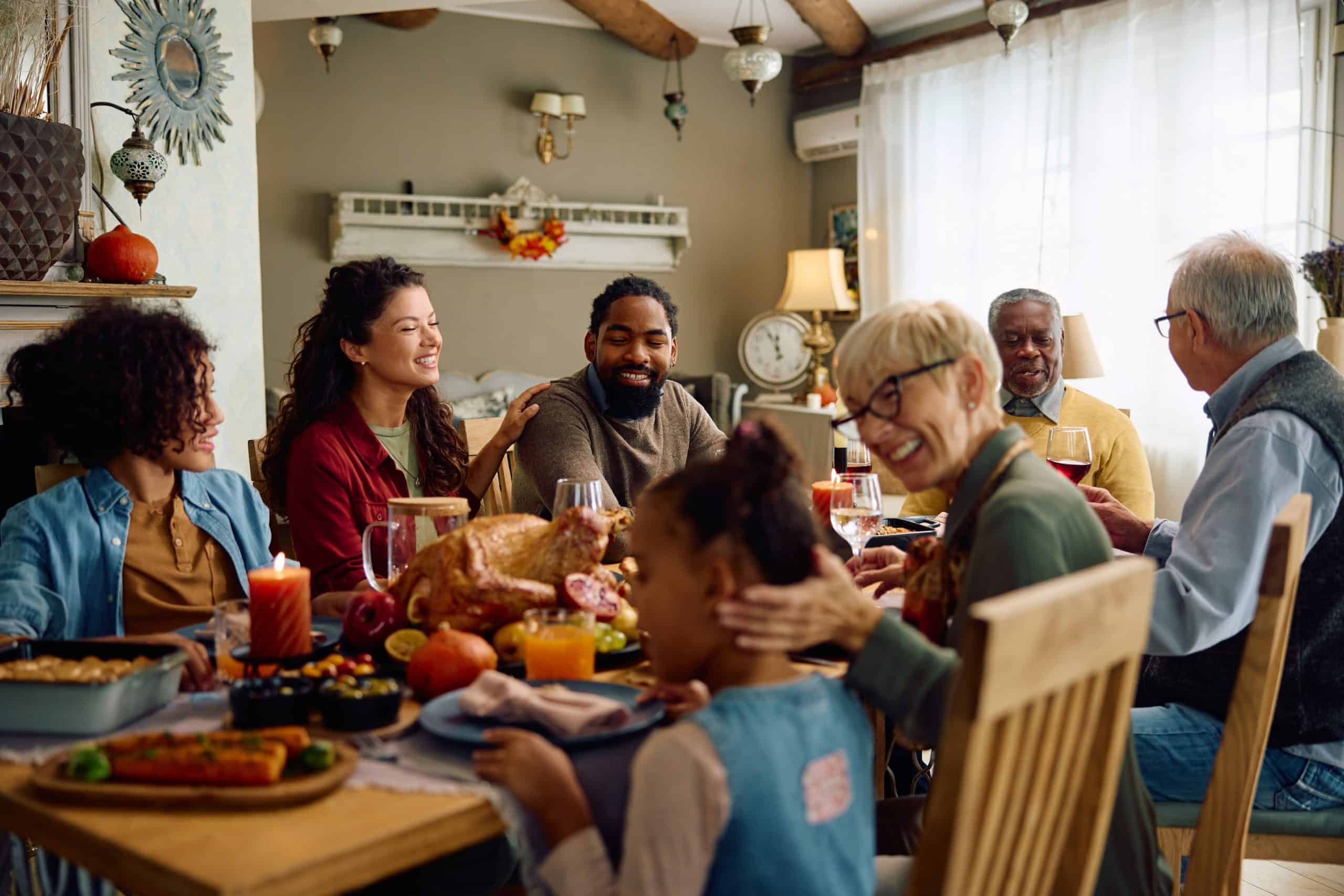 Happy multigeneration family gathering for Thanksgiving meal at dining table.