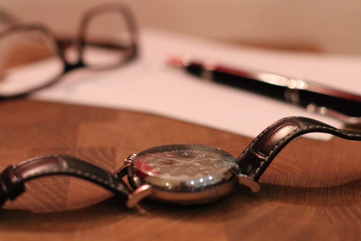 Vintage Longine watch, Montegrappa pen and glasses on wood table. Close up blurred bokeh background. Luxury items on wood desk