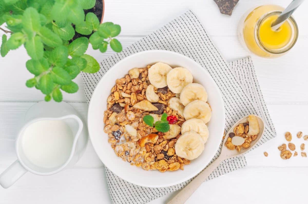 Healthy breakfast with granola in the bowl with banana and nuts on white wooden background. Top view, flat lay.