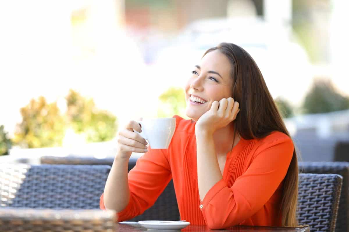 Happy woman thinking drinking coffee sitting in a resturant terrace