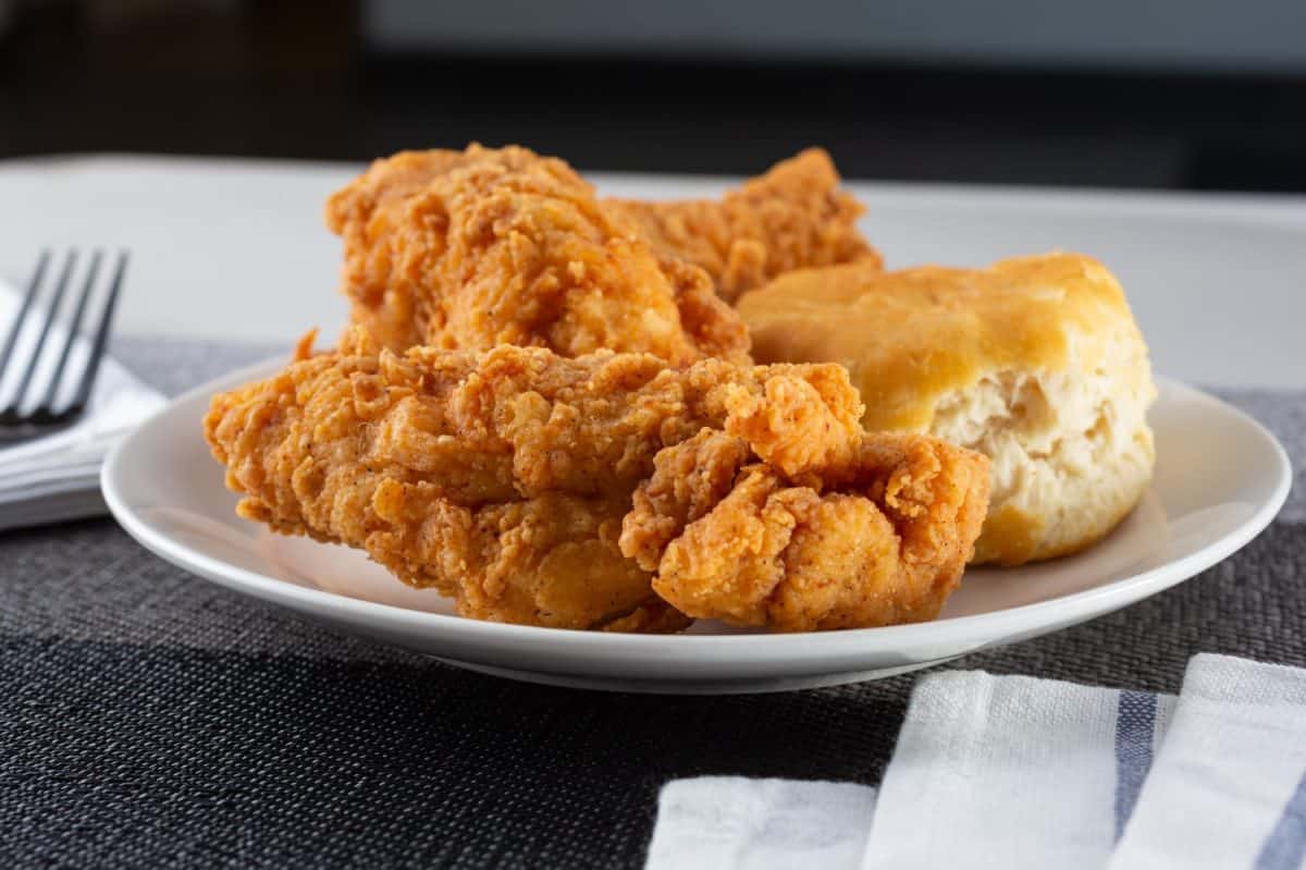 A view of a plate of fried chicken and a biscuit.