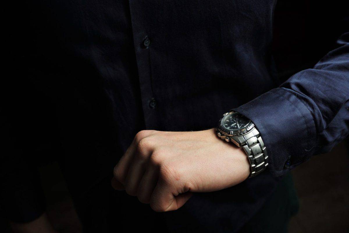 A man in an elegant dark-navy blue shirt checks the time on a prestigious wrist watch