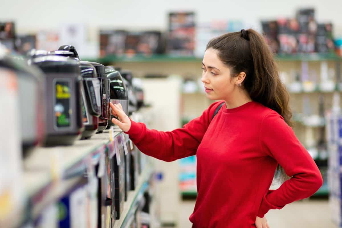 Portrait of young woman chooses a slow cooker in a home appliance store. Side view. The concept of consumerism and shopping.