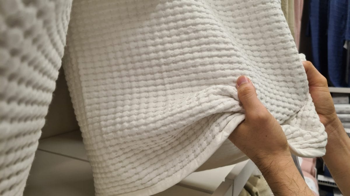 two hand holding a white blanket hanging in a shop.