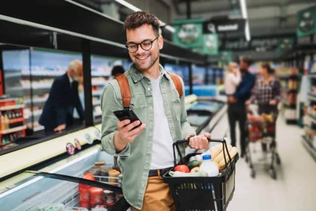 Young man buying groceries at the supermarket. Other customers in background. Consumerism concept.