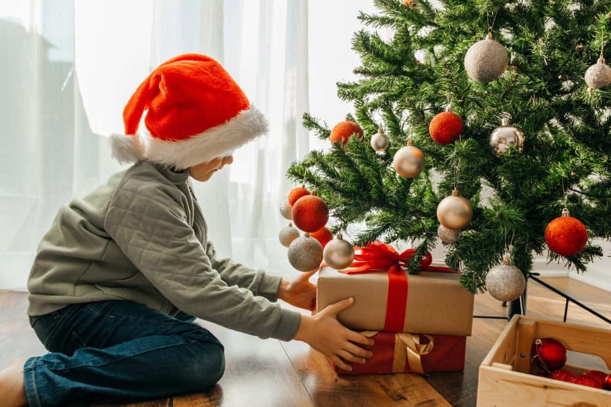 A boy, a child takes out a Christmas present from under the New Year tree, a box with a red ribbon. Children celebrate New Year and Christmas