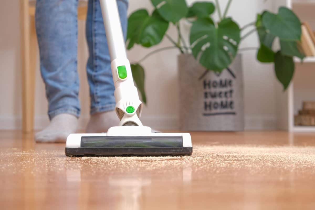 Cleaning room with modern wireless vacuum cleaner without cord. Man in jeans is cleaning floor with modern cordless vacuum cleaner without cord. Man removes sawdust from floor with vacuum cleaner.