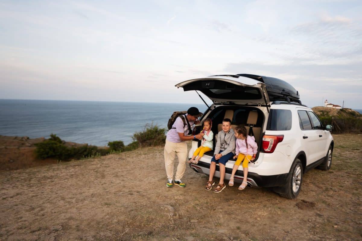 Happy family sitting in the trunk of a camper suv car at the beach. Cape Emine, Black sea coast, Bulgaria.