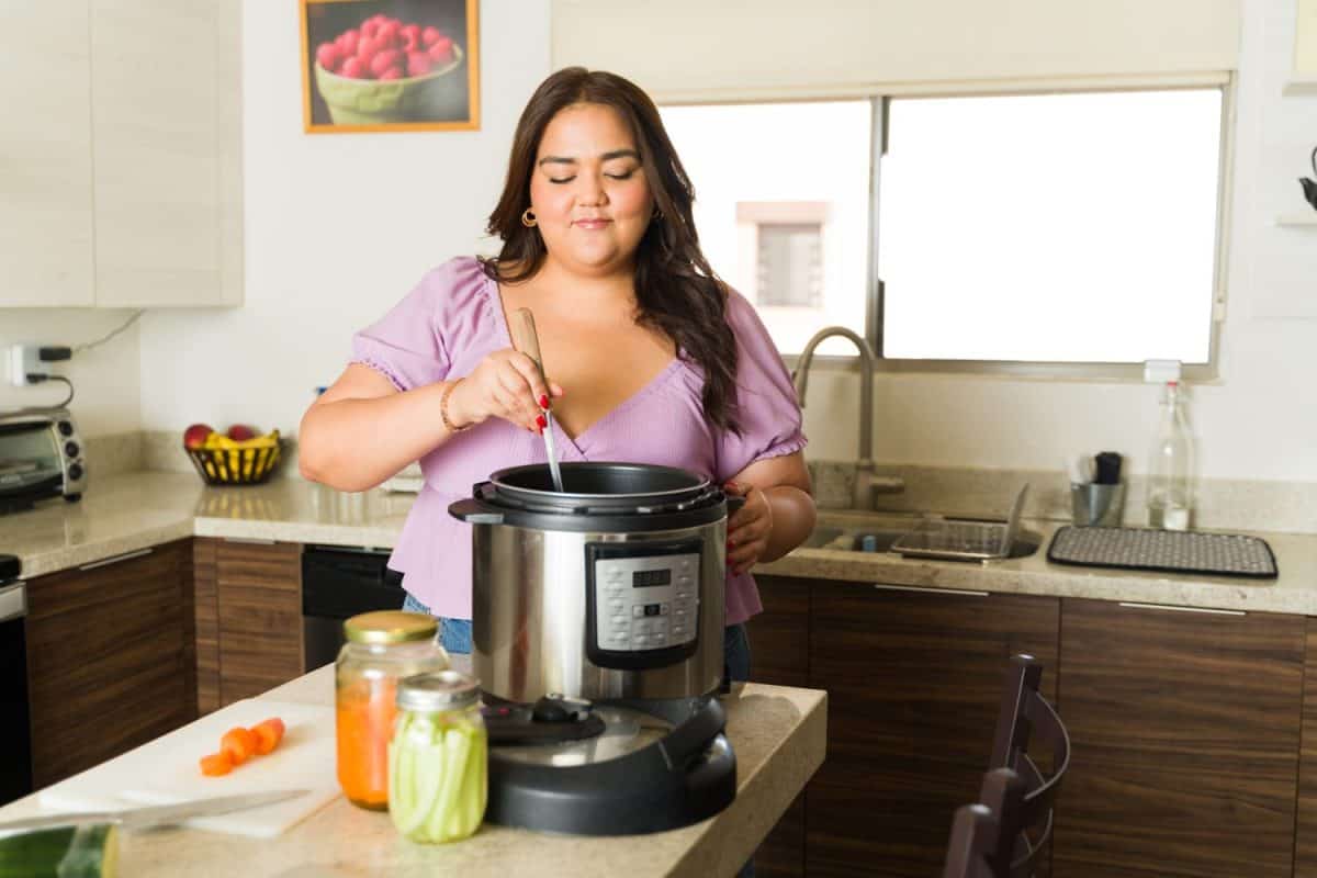 Beautiful plus size woman preparing food lunch in the pressure cooker or slow cooking pot and smiling looking happy doing housework in the kitchen. The Instant Pot Was My Kitchen Hero, But These 16 Appliances Are Superior