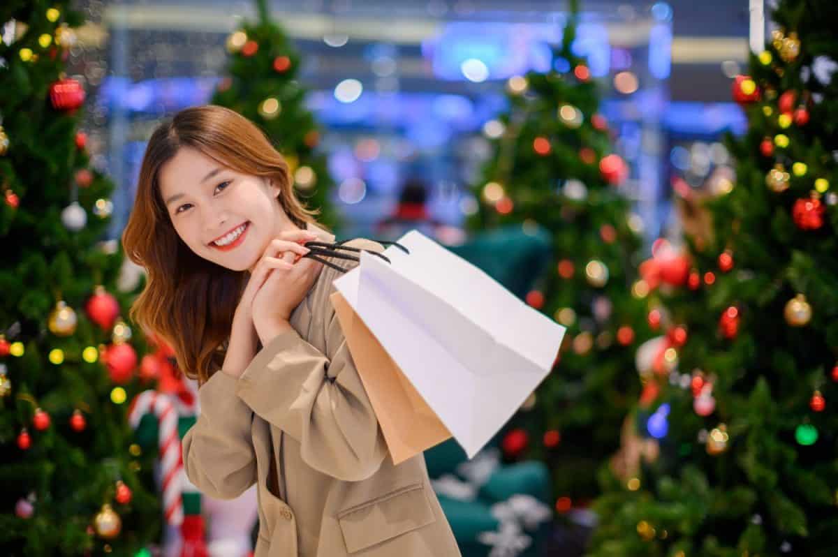 Beautiful asian girl hold shopping bags on Christmas tree bokeh light background at night, happy new year vibes concept