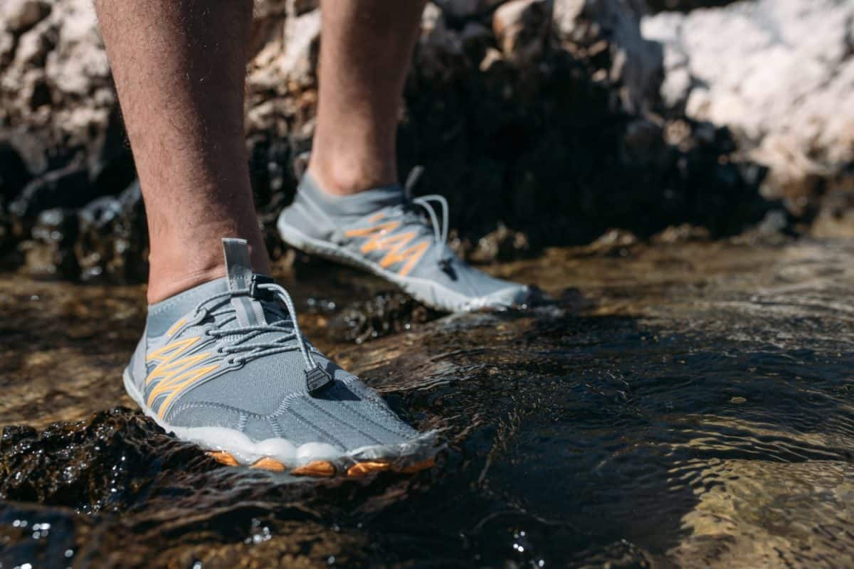 Protective swimming shoes on men's feet. Close-up. Men's feet in stylish sports water slippers on the rocky seashore.