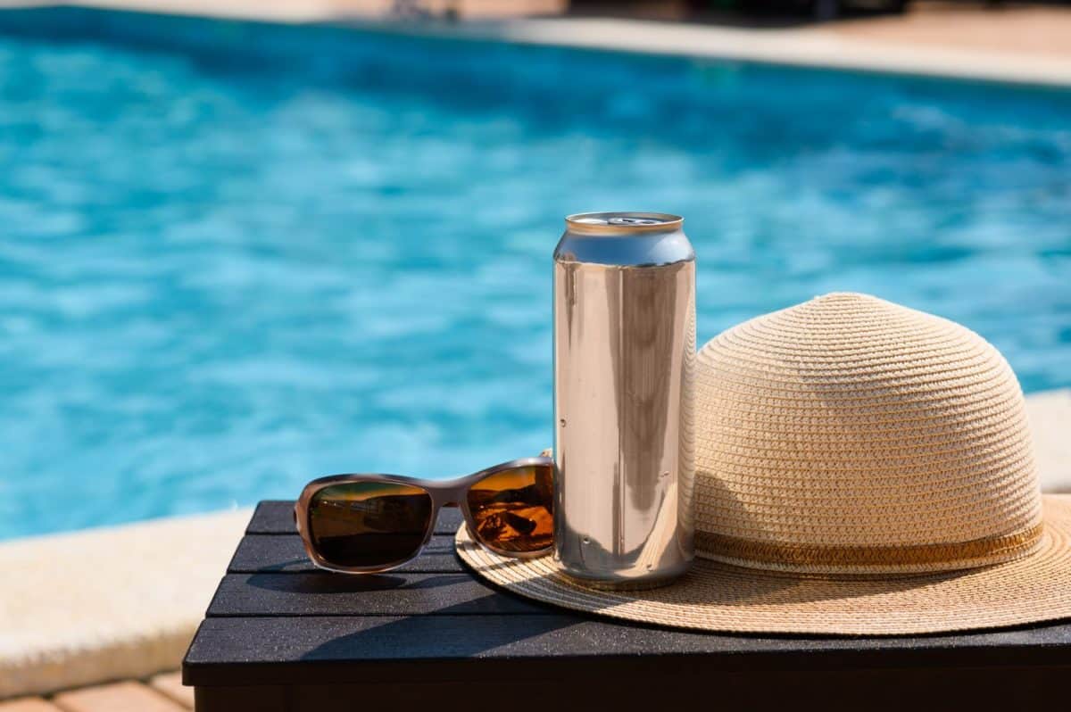 A can of drink and a straw hat near the pool at a resort. Relaxing summer holiday by the pool