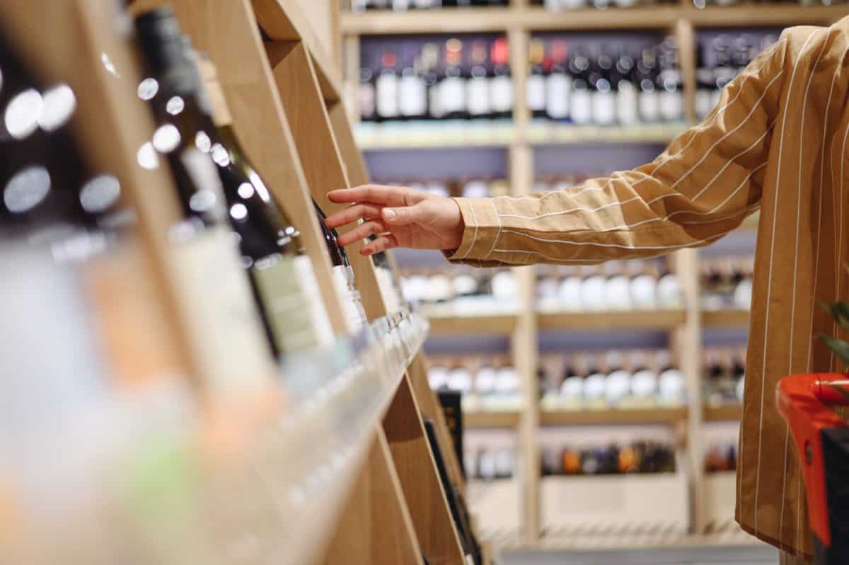 Sideways close up young customer woman wear casual clothes choosing alcohol wine bottle shopping at supermaket store grocery shop buying products inside hypermarket. Purchasing food gastronomy concept