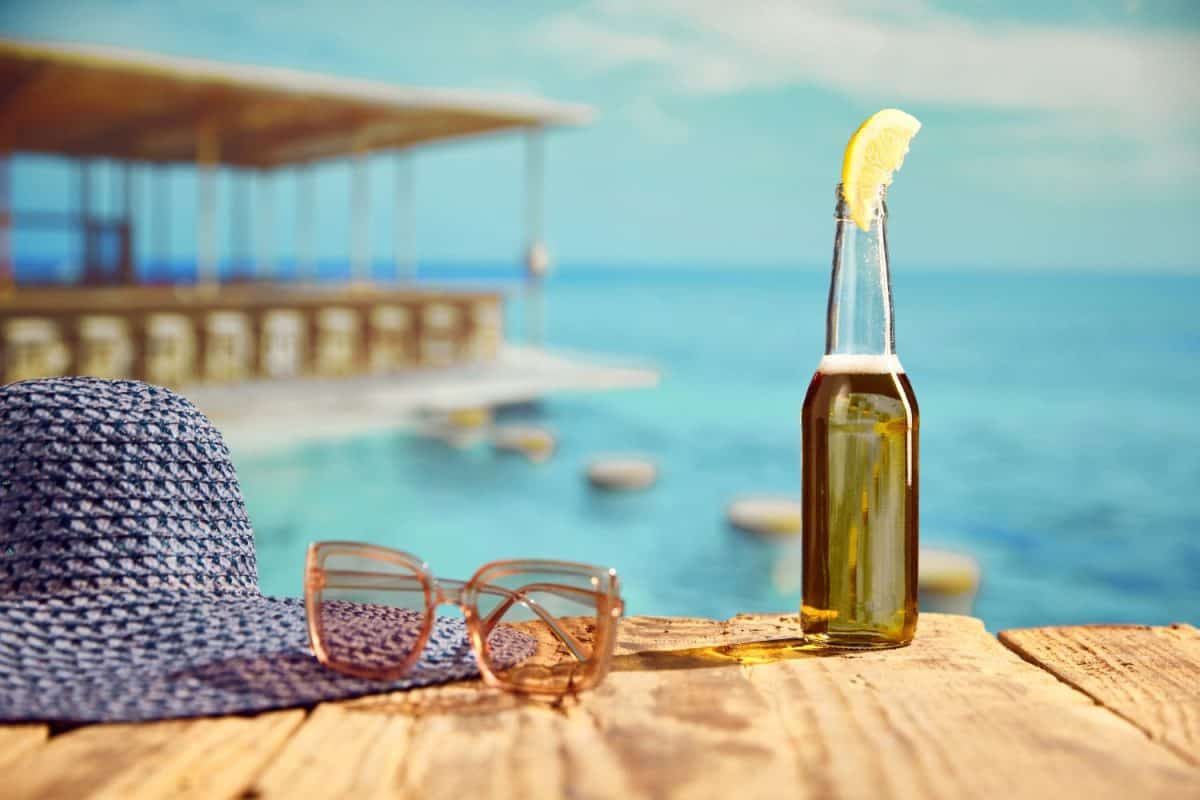 Bottle of light beer with slice of lemon standing on wooden table on beach bar with sea background. Concept of summer, vacation, relaxation, travelling, leisure time