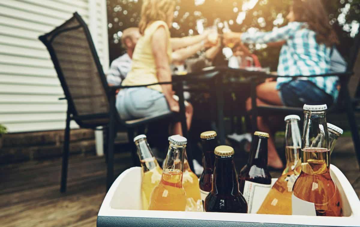 Group, people and drinks at barbecue in backyard, summer and vacation for holiday, celebration or event. Friends, cheerful and bbq with cooler box for dinner, party or reunion with alcohol in America. 8 Coolers That Are Cheaper and Just as Good as a Yeti