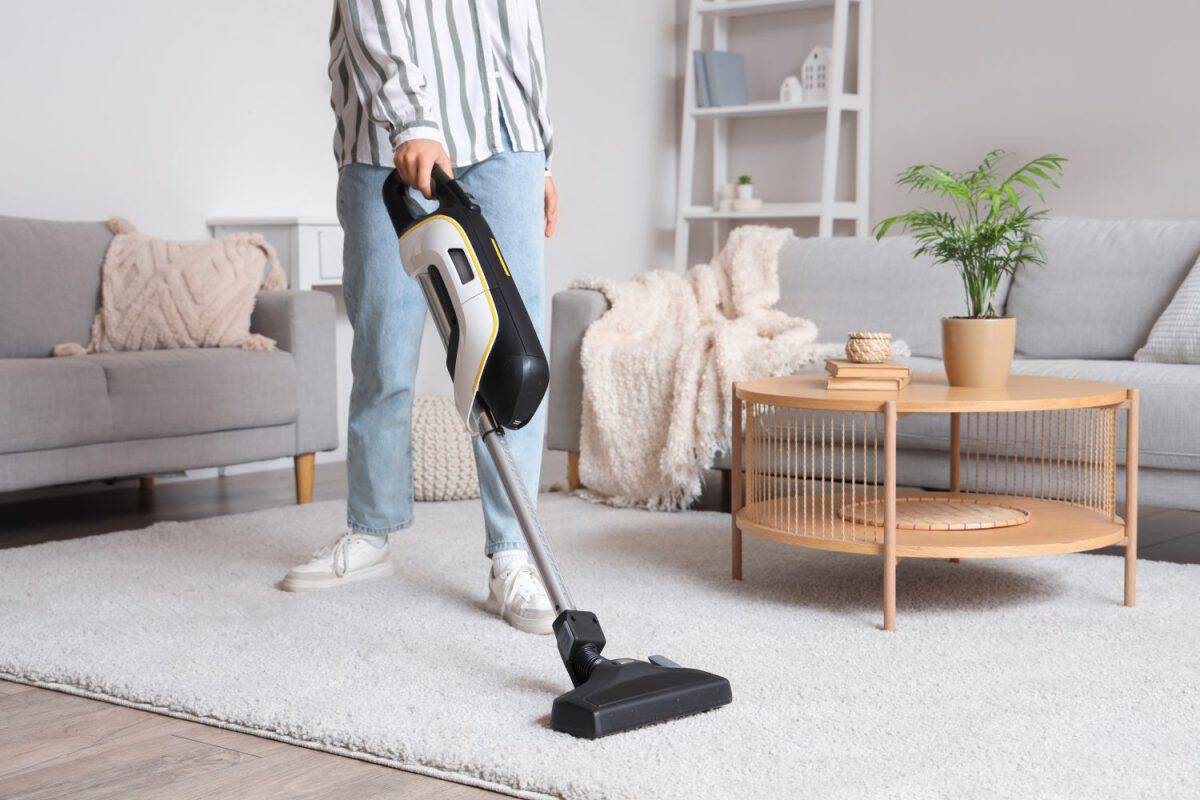 Young woman cleaning carpet with cordless stick vacuum cleaner in living room