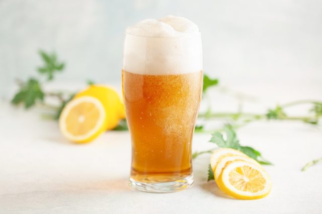 Boozy Refresing Cold Lemon Beer or Radler in a Pint Glass on the table.