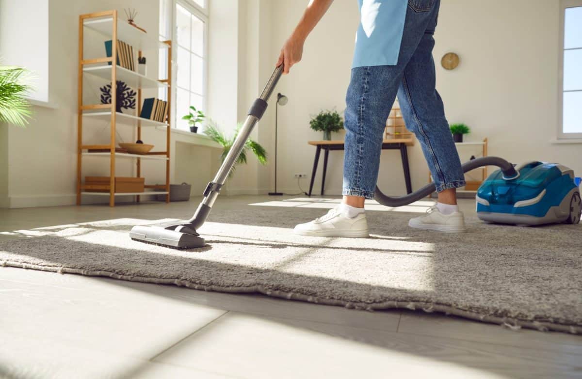 Cropped photo of woman cleaning with vacuum cleaner carpet in the living room at home. Female janitor vacuuming the floor. Cleaning service, housekeeping, housework and household concept.