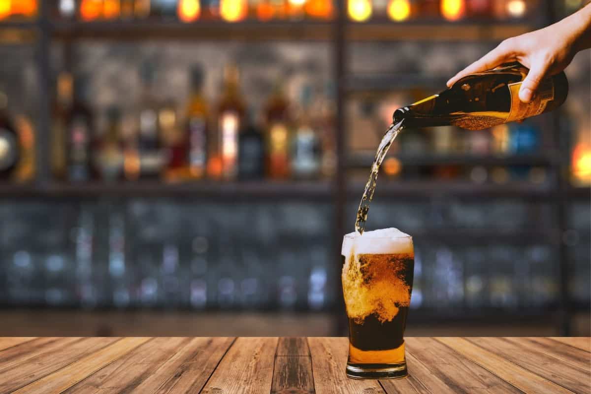 Picture of a person holding a beer bottle pouring beer into a glass. In the background is a bar. Suitable for use Food and beverage media and advertising media.