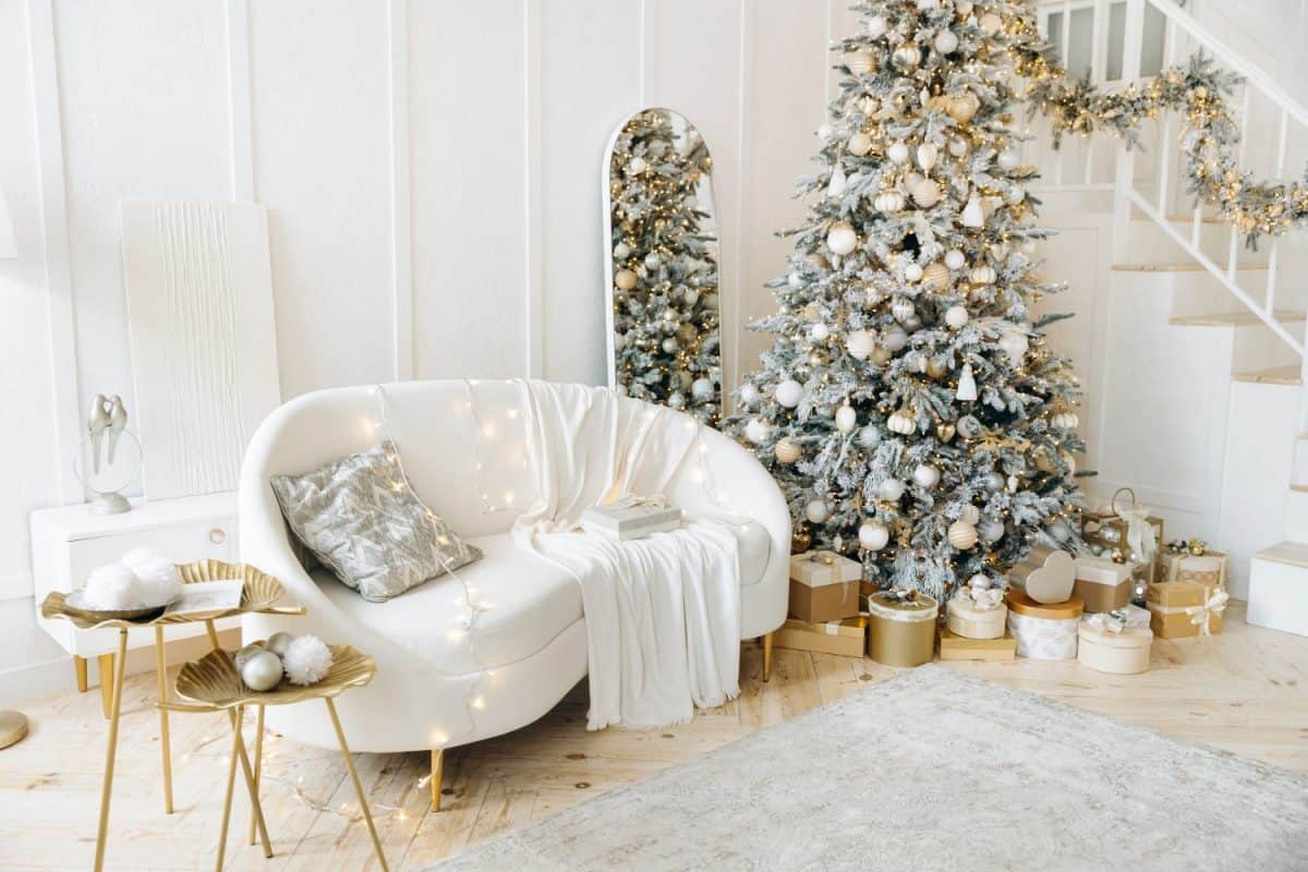 Room with Christmas decorations, white sofa adorned with lights, cozy blanket, Christmas tree decorated with ornaments, gold gift boxes, staircase, elegant and festive