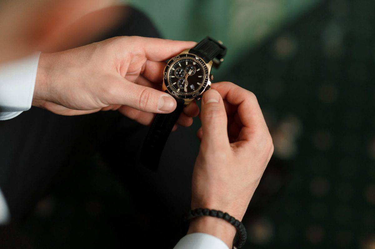 A man is wearing a watch and is adjusting it. The watch is black and gold