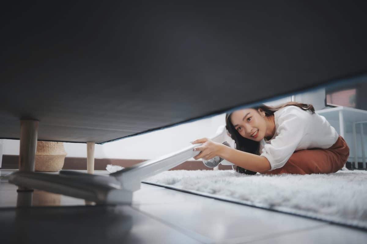 Woman is vacuuming her living room, reaching under the sofa to clean every corner