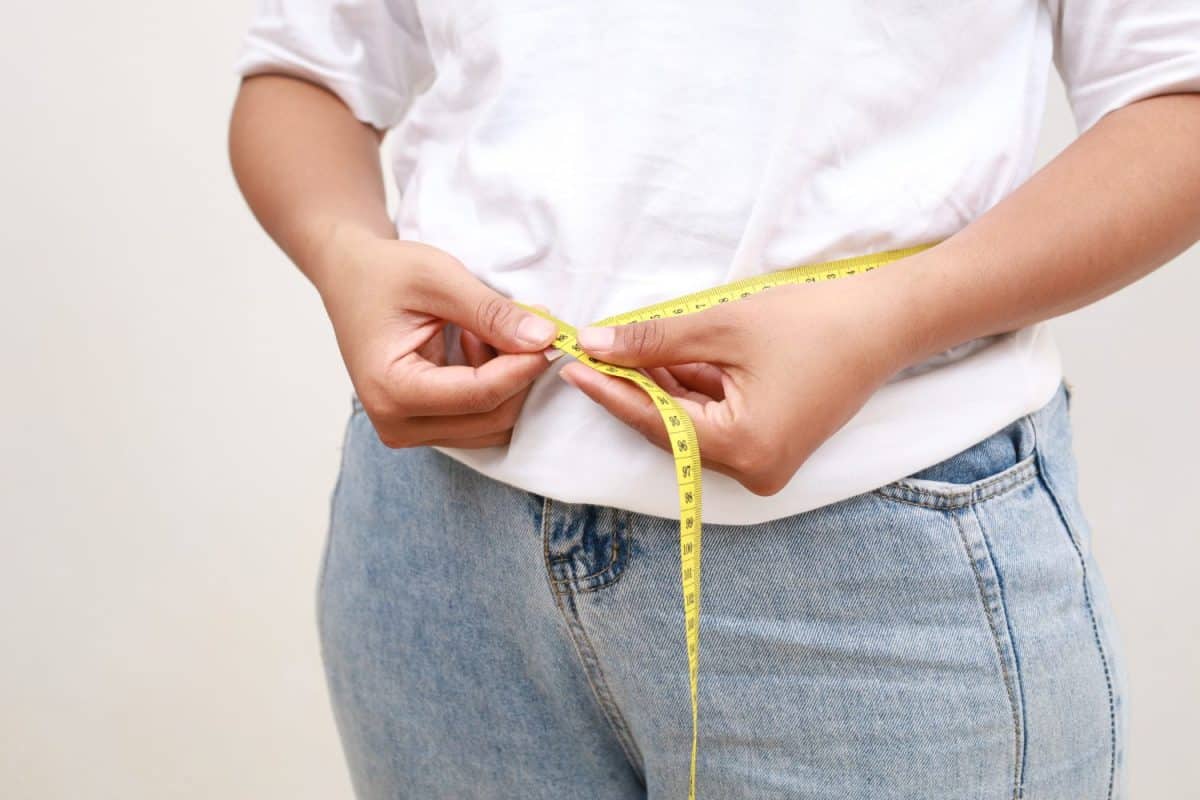 Close up woman in white shirt measuring her waist with yellow measuring tape. Weight loss, slim body, healthy lifestyle concept. Figure control and counting calories. Successful diet plan. In-N-Out vs. Shake Shack: Who Actually Has the Better Burger?