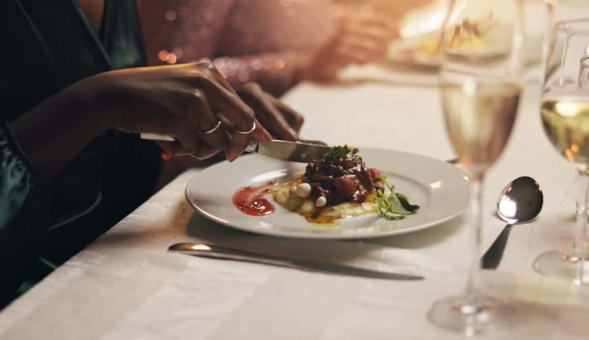 Hands, dinner and plate of food at party for nutrition, health and knife for meat with charity drive at night. Person, meal and diet with luxury, fundraiser and fine dining with drinks at gala