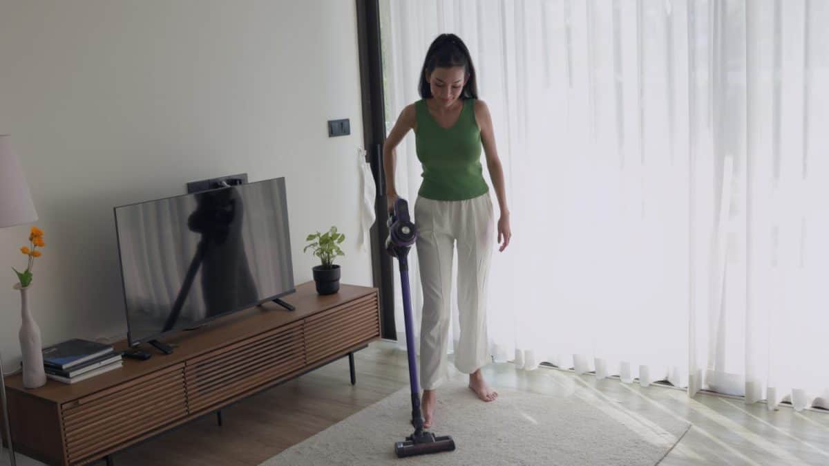 Woman cleaning the floor with a vacuum in a modern living room. I Loved My Dyson But These 8 Vacuum Brands Are a Better Deal